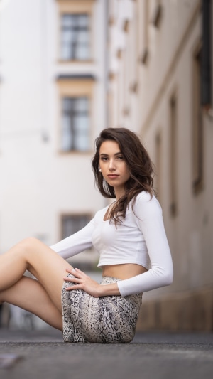 Model in white top and snake print skirt sitting on ground