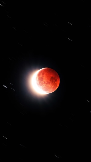 Red moon during a lunar eclipse with star trails