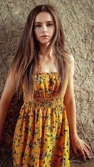 Woman in yellow floral dress against stone wall