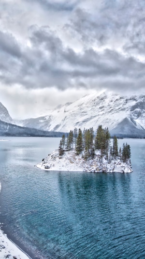 Winter island with trees on a lake with snowy mountains
