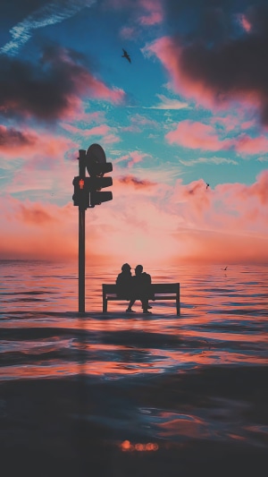 Couple on bench by traffic light in ocean at sunset 4K