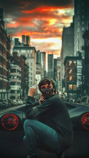 Person in mask and beanie crouching by a car in a city
