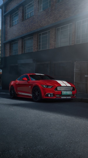 Red Ford Mustang with white stripes parked on street