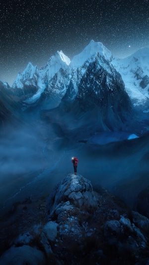 Man with headlamp on mountain peak under starry sky