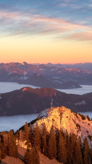 Mountain summit with cross at sunrise over clouds