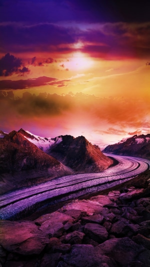 Glacier winding through mountains under a colorful sunset sky