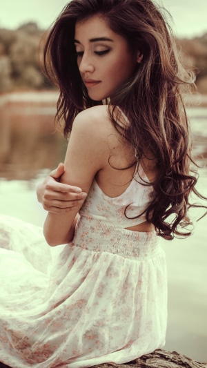 Woman in white floral dress sitting by water