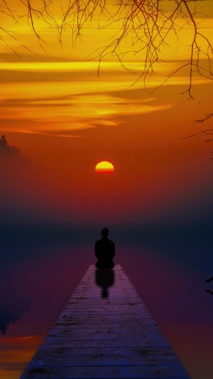 Silhouette meditating on a pier at sunset