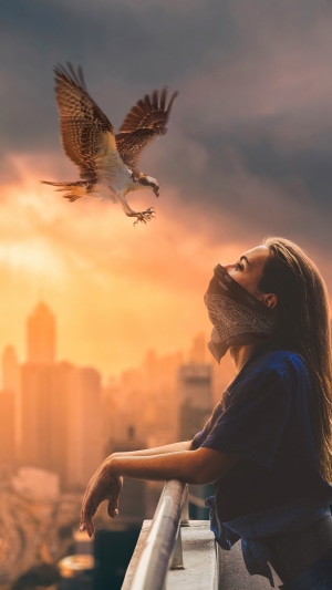 Woman and hawk in front of city skyline at sunset