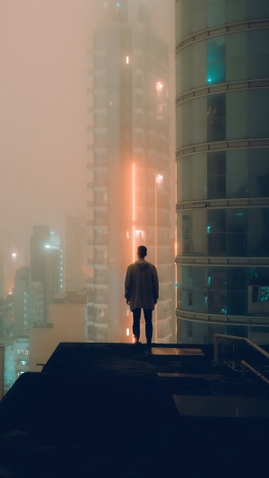 Man standing on a rooftop overlooking a foggy city at night
