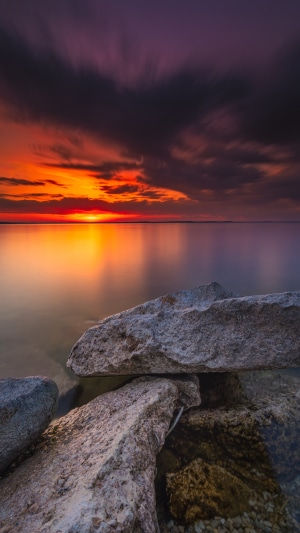 Sunset over the water with rocks in the foreground 4K