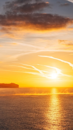 Sunrise over the ocean with clouds and a cliff