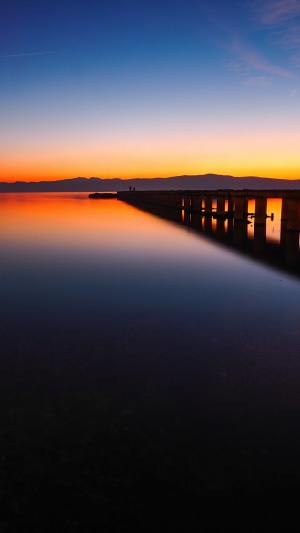 Pier over calm water at sunset with mountains