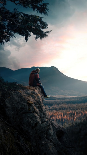 Man sitting on a cliff overlooking mountains