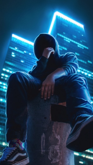 Hooded figure sitting in front of a neon-lit skyscraper