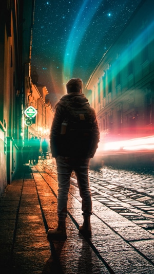 Man standing on cobblestone street at night with aurora