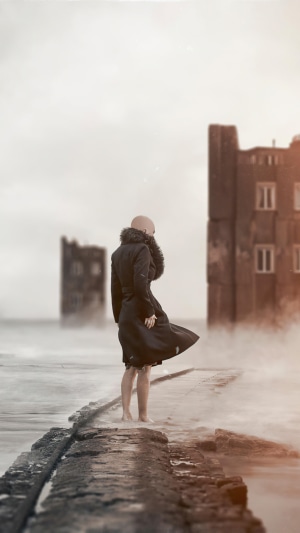 Bald person in black coat on pier with buildings in fog