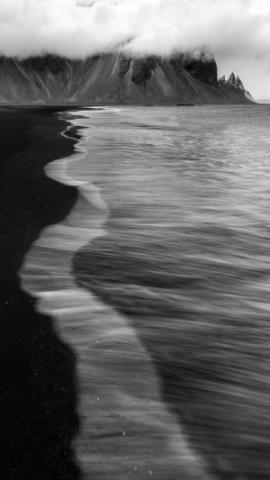 Black sand beach with waves and mountains
