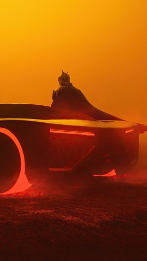 Batman sitting on the Batmobile in a foggy orange environment