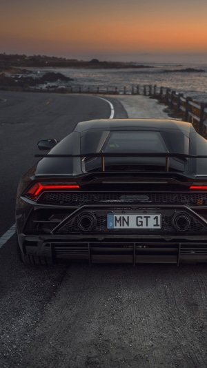 Black Lamborghini Huracan Evo on a coastal road at sunset