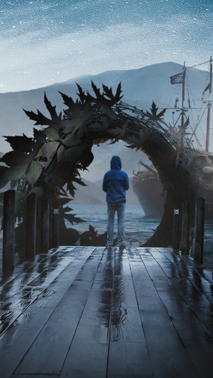 Person in hoodie on a wet pier with a ship in the background