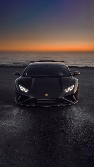 Black Lamborghini Huracan Evo on a road by the ocean at sunset