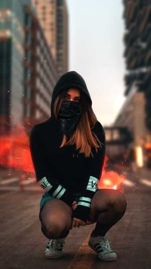 Girl in hoodie and bandana crouching in city
