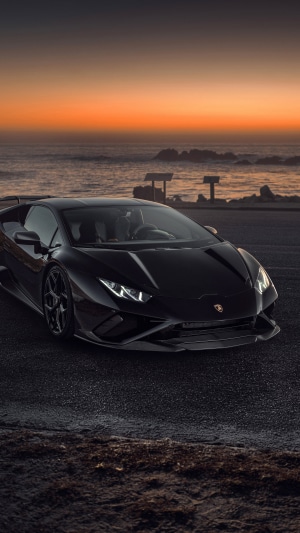 Black Lamborghini Huracan Evo parked by the ocean at sunset