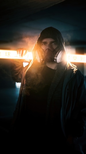 Man in gas mask and hoodie holding glowing sign