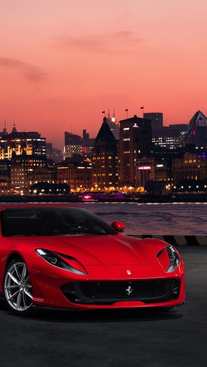 Red Ferrari 812 Superfast in front of city skyline at dusk