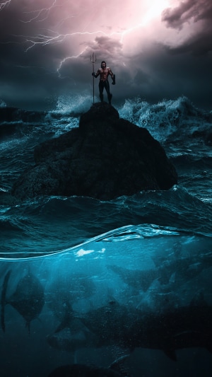 Aquaman standing on a rock in the ocean with sharks below