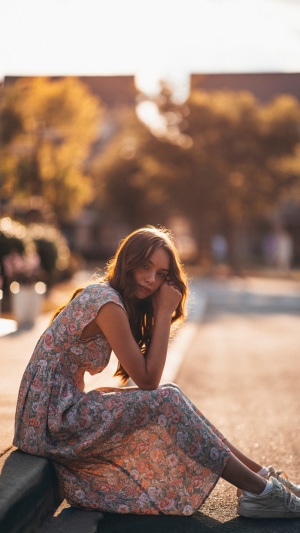 Girl in floral dress sitting on curb