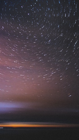 Star trails over a dark landscape and ocean
