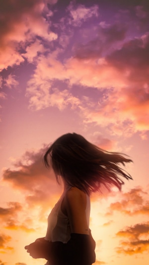 Girl with windblown hair against colorful sunset clouds
