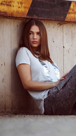 Model in t-shirt and jeans leaning against concrete wall