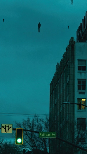 Figures floating in the sky above a city street