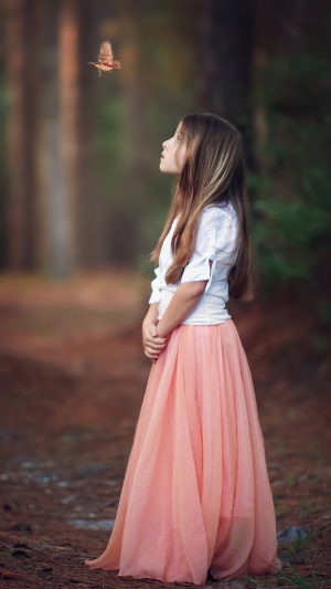 Little girl looking at a bird in a forest