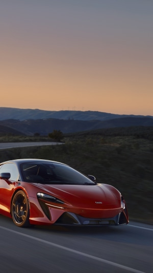 Red McLaren Artura driving on a road at sunset
