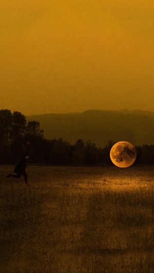 Person running towards a large moon in a field