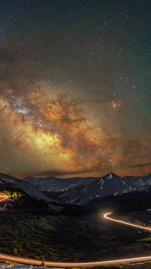 Milky Way over mountains with light trails on road