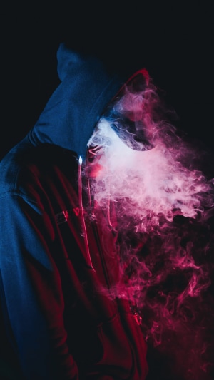 Person in a hoodie exhaling colorful smoke