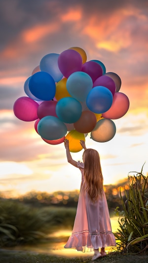 Little girl holding colorful balloons at sunset