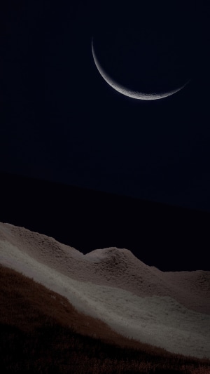 Crescent moon over rolling hills at night