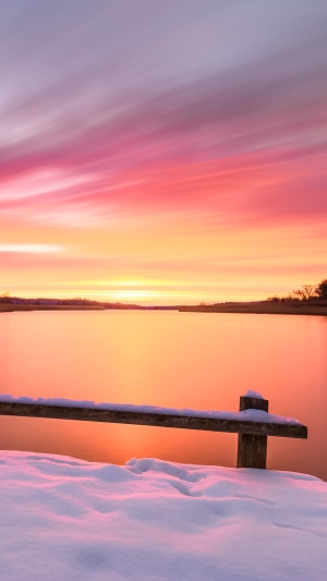 Winter sunrise over a snowy lake with wooden pier