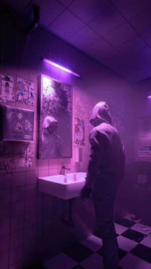 Hooded figure in a purple-lit bathroom