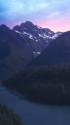 Snow-capped mountains over a dark forest and lake