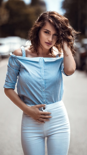 Model with curly hair wearing a blue off-the-shoulder shirt and white pants