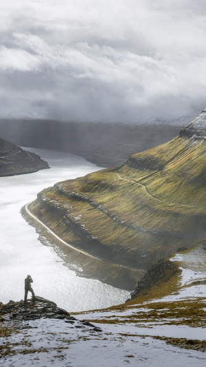 Photographer on cliff overlooking a fjord and mountains