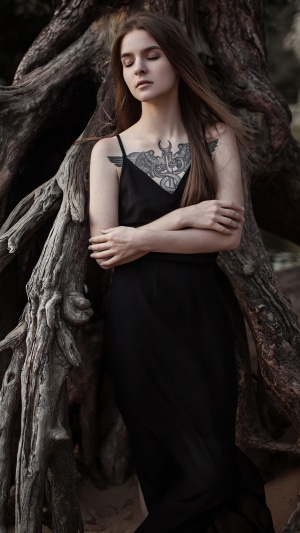 Woman with tattoo in black dress near tree roots