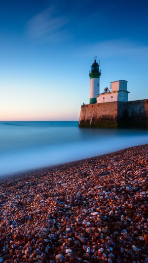Lighthouse on a stone pier by the ocean at dusk